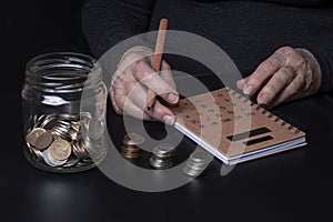 The concept of poverty in old age. An elderly woman planning her budget. Bank with coins on dark background