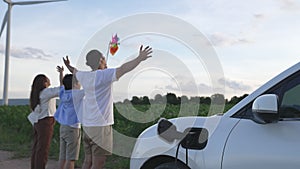 Concept of progressive happy family at wind farm with electric vehicle.