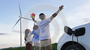 Concept of progressive happy family at wind farm with electric vehicle.