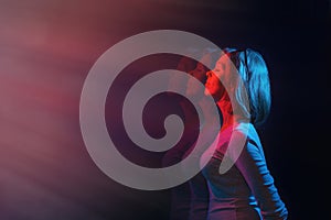 The concept of psychology and perception. The woman stands in profile, eyes closed, against a black background. Blue and red light