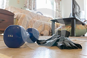 Concept quarantine home training set - 5 kg dumbbell and pair of gloves on floor near couch