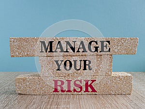 Concept red word Manage your risk on brick blocks. Beautiful blue background, wooden table. Business and manage your risk concept