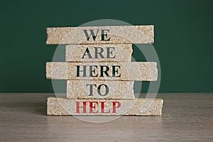 Concept red words we are here to help on brick blocks. Beautiful green background, wooden table. Business concept