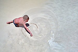 Concept of relaxation at sea. Cute boy on seashore paints smiling sun on sand. Child paints smiley face. Top view, copy space.