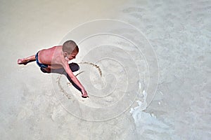 Concept of relaxation at sea. Little boy on seashore paints smiling sun on sand. Cute child paints smiley face Top view copy space