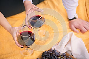 The concept of relaxing a loving couple on a picnic. Female and male hands holding glasses with wine against a background of yello