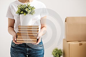 The concept of relocation and moving to a new home. Close-up, female hands hold a pile of books and a green plant in a