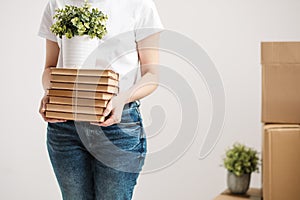 The concept of relocation and moving to a new home. Close-up, female hands hold a pile of books and a green plant in a