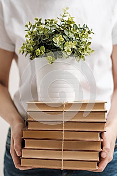 The concept of relocation and moving to a new home. Close-up, female hands hold a pile of books and a green plant in a