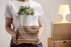 The concept of relocation and moving to a new home. Close-up, female hands hold a pile of books and a green plant in a