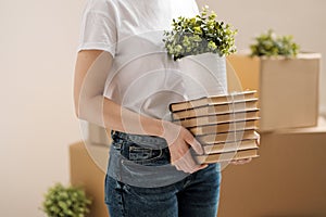 The concept of relocation and moving to a new home. Close-up, female hands hold a pile of books and a green plant in a