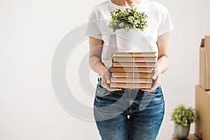 The concept of relocation and moving to a new home. Close-up, female hands hold a pile of books and a green plant in a