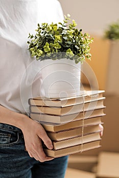 The concept of relocation and moving to a new home. Close-up, female hands hold a pile of books and a green plant in a