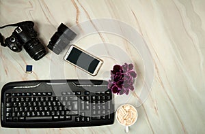 Camera, lens, memory card, keyboard, smartphone and a mug of delicious cocoa with marshmallows on a pastel green marble background