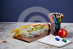 Concept of school lunch break with healthy lunch box and school supplies on wooden desk, selective focus.