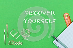 Text discover yourself, school supplies wooden miniatures, notebook on green background
