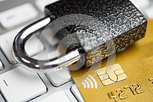 Concept of security of electronic payment. Lock on gold credit card and white keyboard