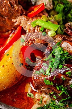 The concept of Serbian cuisine. Juicy baked beef in its own juice with potatoes, vegetables and greens. Serve in an iron fire