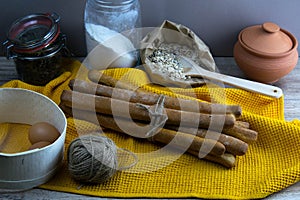 Concept shot of spice bread sticks with a wooden spoon on the wood table, oatmeal and a skein of bag thread, egg, flour, seeds and