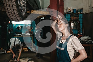 The concept of small business, feminism and women`s equality. A young female auto mechanic wearily wipes sweat from her forehead