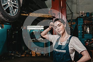 The concept of small business, feminism and women`s equality. A young woman mechanic wipes sweat from her forehead, on the lift i