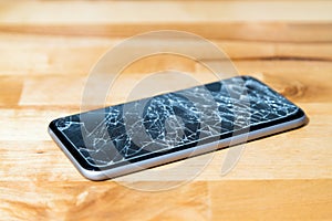 Concept of smart phone with broken screen. Top view on wooden desk background. Cracked, shattered lcd touch screen on modern