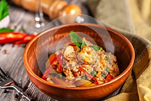 Concept of Spanish cuisine. Paella with seafood and shrimps, with green peas in a clay plate. A glass of cool wine is on table