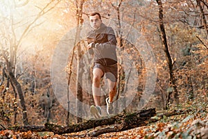 Concept of sport and active lifestyle. A young man Jogging in the autumn forest. Jump over the log