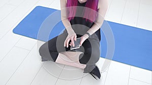 Concept of sport and fitness. Young sportswoman sitting and using fitness tracker and smartphone