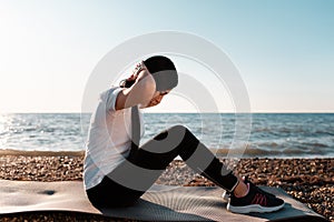 Concept of sport and healthy lifestyle. Woman in sportswear is training on the Mat. In the background, a rocky shore and the sea.