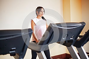 Concept of sport and healthy lifestyle. Young attractive fitness woman running on treadmill, wearing in white sportswear