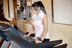 Concept of sport and healthy lifestyle. Young attractive fitness woman running on treadmill, wearing in white sportswear