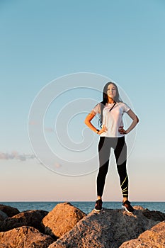 The concept of sport and a healthy lifestyle. A young woman in sportswear , standing on the coastal rocks, hands on hips. Copy