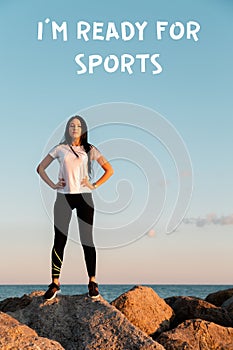 The concept of sport and a healthy lifestyle. A young woman in sportswear , standing on the coastal rocks, hands on hips. Text I`