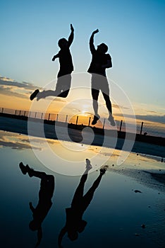 Concept: sport. Two sporty people outdoors. Silhouette of two unrecognizable men jumping to high ground. Sunset with epic sky.
