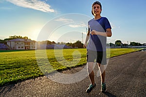 Concept of sports and health - teen boy runs along the stadium track, a soccer field with green grass