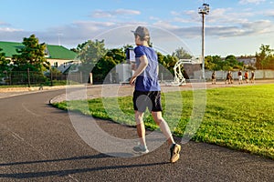 Concept of sports and health - teen boy runs along the stadium track, a soccer field with green grass