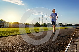 Concept of sports and health - teen boy runs along the stadium track, a soccer field with green grass