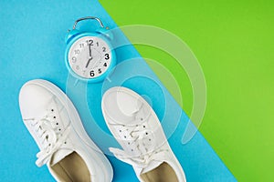 The concept of sports, jogging. Photo from above of white rosettes with an alarm clock on a two tone green and blue background