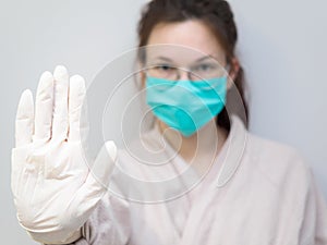 Concept: stop coronavirus, ncov-19, epidemic, pandemic. A young European woman in rubber gloves and a protective mask holds out photo