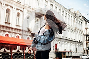 The concept of street fashion. Young beautiful model in the city. Dynamically young girl walks down the street.Hair fluttering in