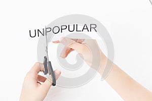 The concept of success and self-development. Female hands scissor the word unpopular photo