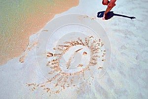 Concept of summer rest by the sea. On the seashore in the sand painted a smiling sun. Smiley on the sand in the surf line.