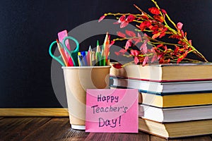 Concept of Teacher's Day. Objects on a chalkboard background. Books, green apple, plaque: Happy Teacher's Day, pencils and pens