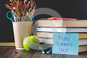 Concept of Teacher's Day. Objects on a chalkboard background. Books, green apple, plaque: Happy Teacher's Day, pencils and pens