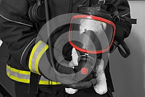 The concept of teaching children in the event of a fire: a firefighter holds a teddy bear in a breathing mask in his hands