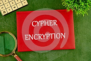 The concept of technology and development. The CYPHER ENCRYPTION concept phrase on the cover of a red notebook on a green photo