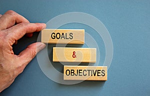 Concept text `goals and objectives` on wooden blocks on a beautiful blue background. Male hand. Copy space. Business concept