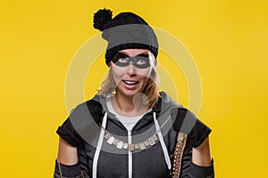 The concept of theft. A blonde woman in a hat, mask and gloves holds the jewels in both hands and happily puts them on. Yellow