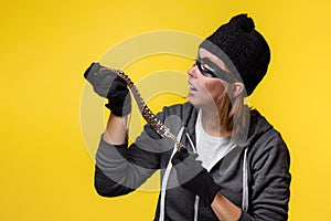 The concept of theft. A woman in a hat, mask and gloves holds the jewels in both hands and looks at them in surprise. Yellow